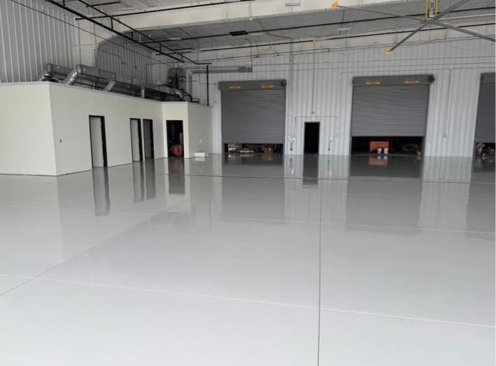 Spacious empty warehouse featuring a polished light gray epoxy floor and industrial roll-up doors.
