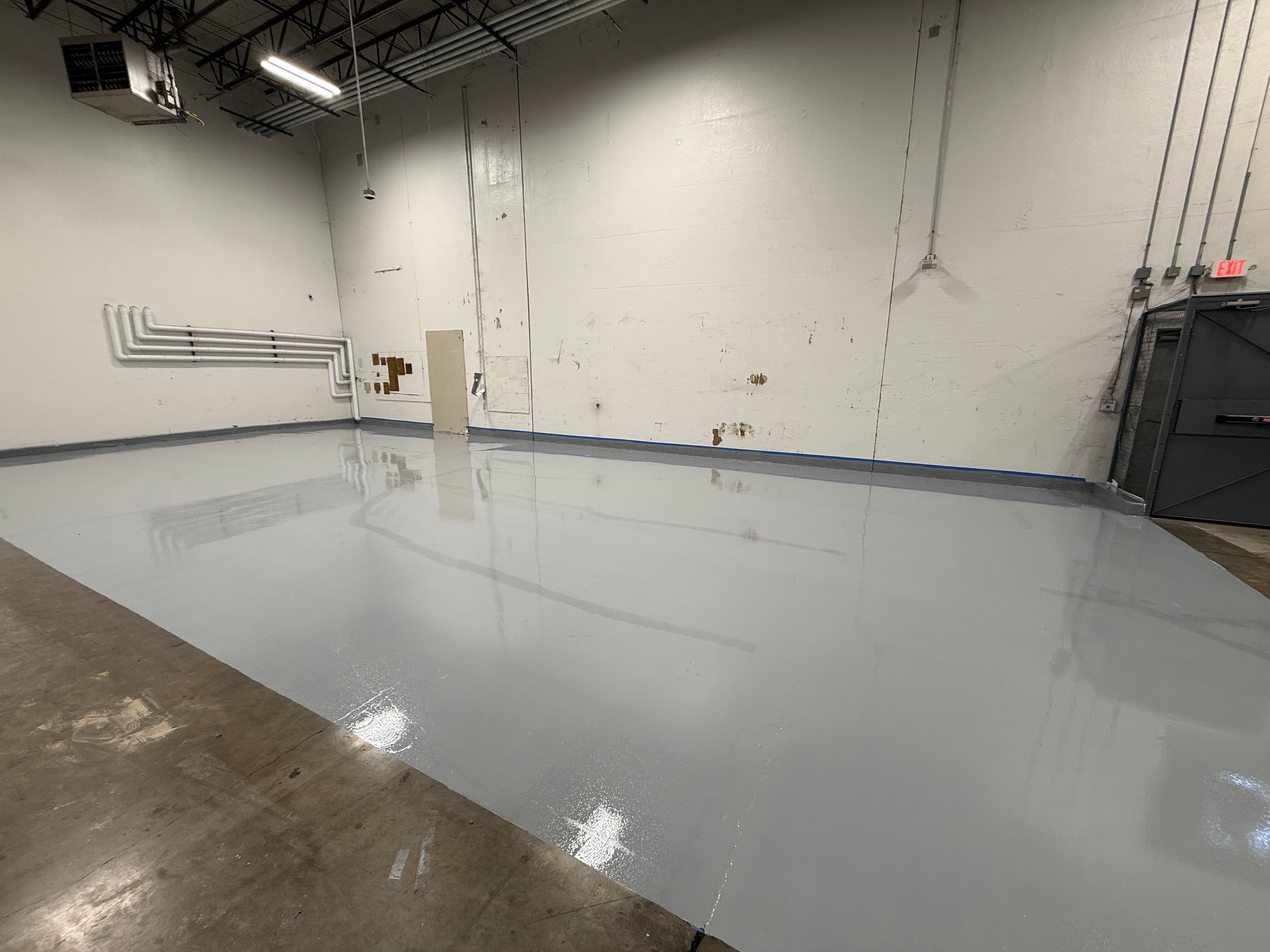 Freshly applied glossy grey epoxy floor coating in a large, empty industrial warehouse space.