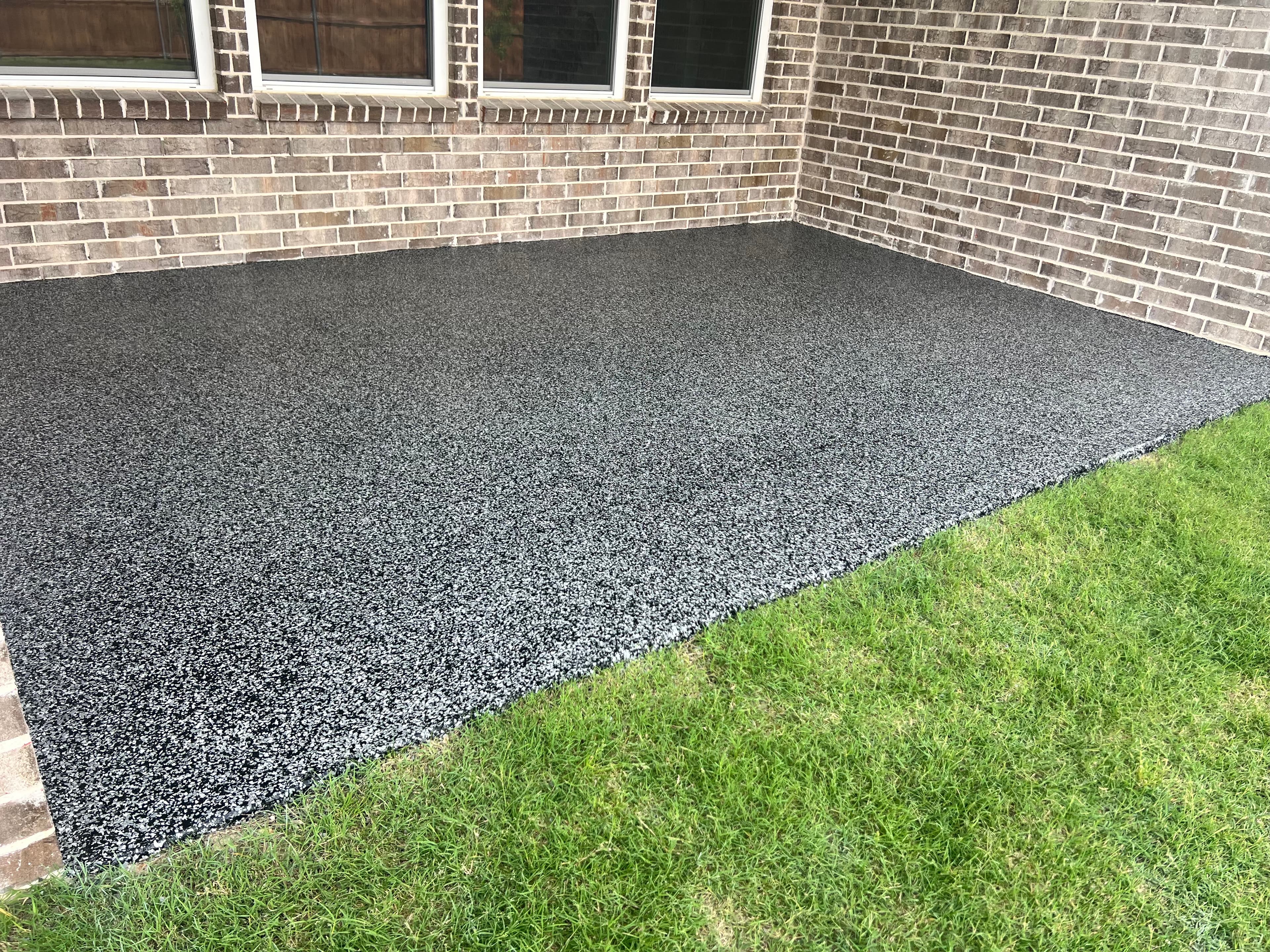 Grey and black speckled epoxy patio floor next to a brick wall and green grass.