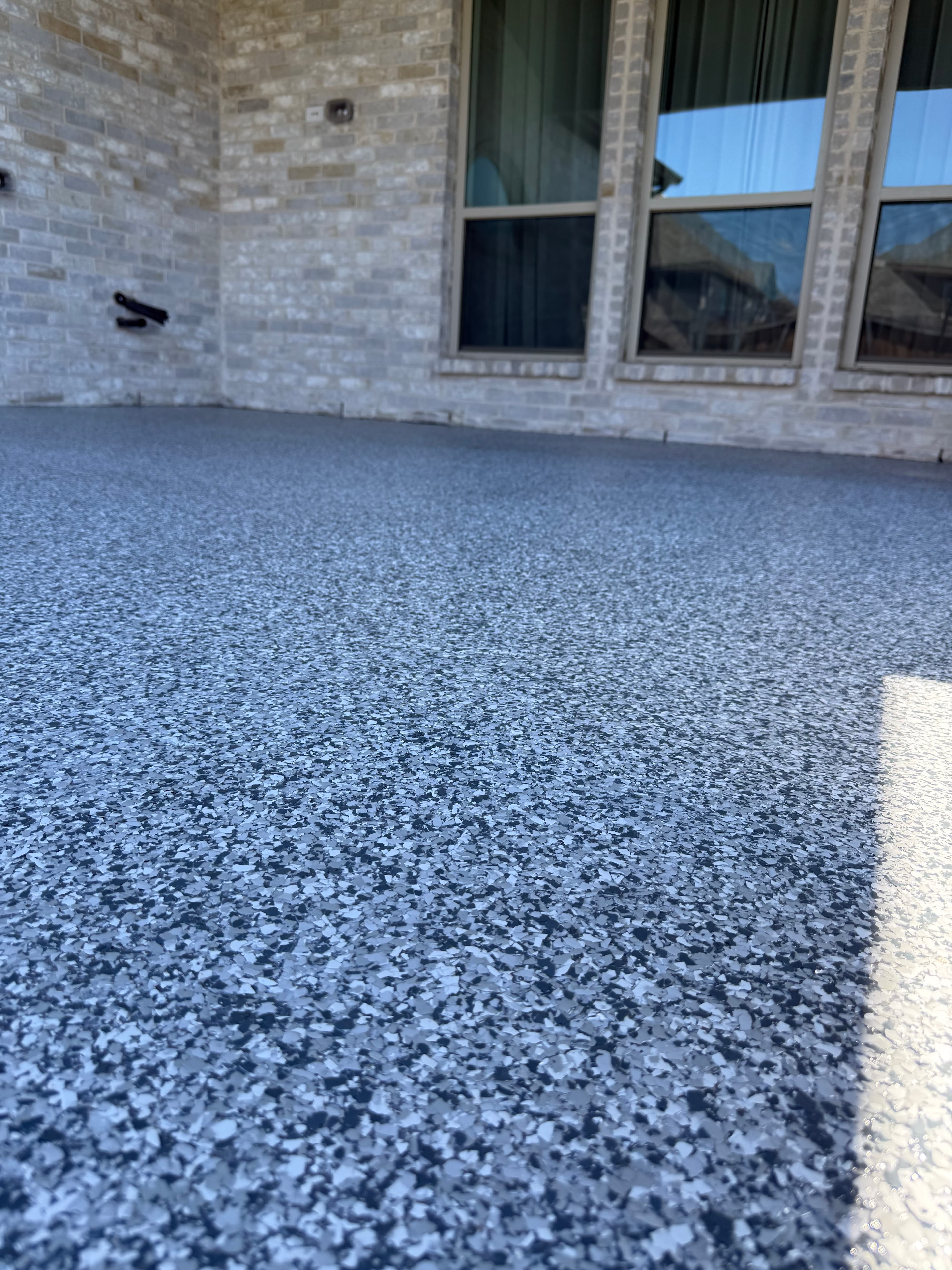 Grey speckled floor coating with black and white flakes next to a light brick wall.