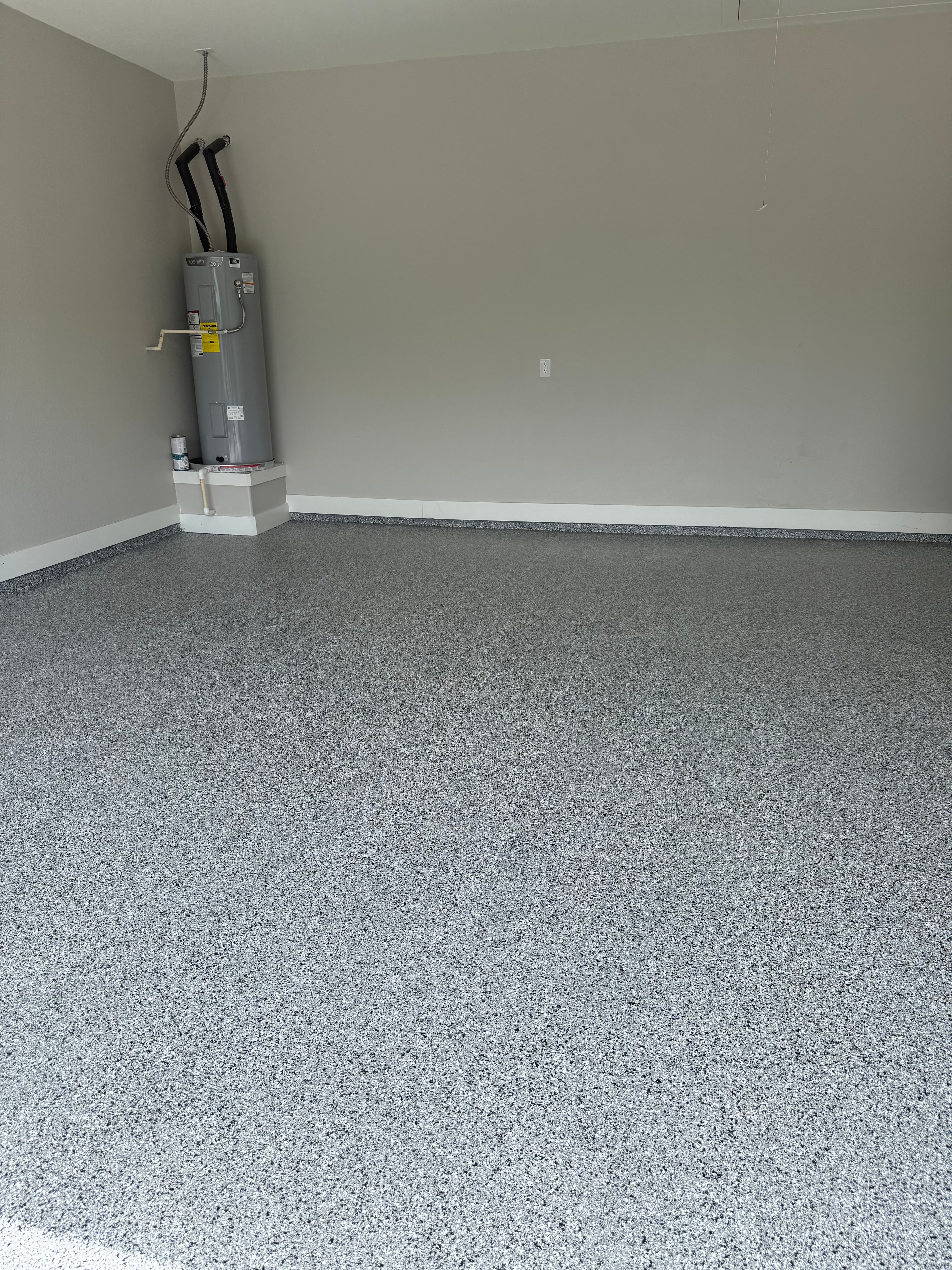 Grey speckled epoxy floor in a garage with a water heater against a light wall.