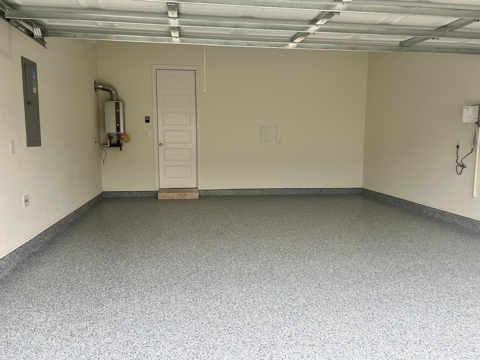 Empty garage with a grey speckled epoxy floor, white walls, and a tankless water heater.