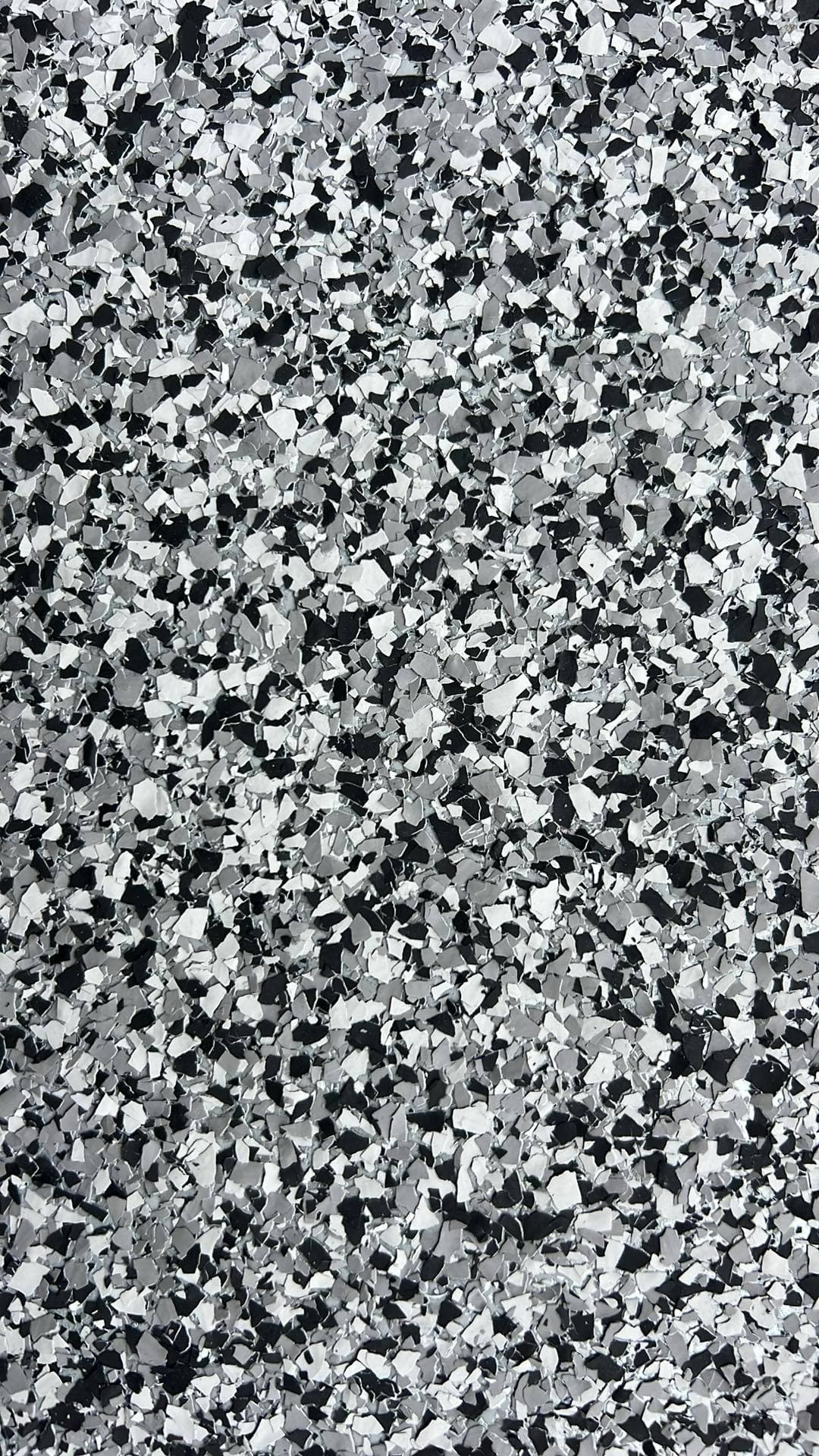 Close-up of black, white, and gray decorative flakes scattered across a textured epoxy floor.